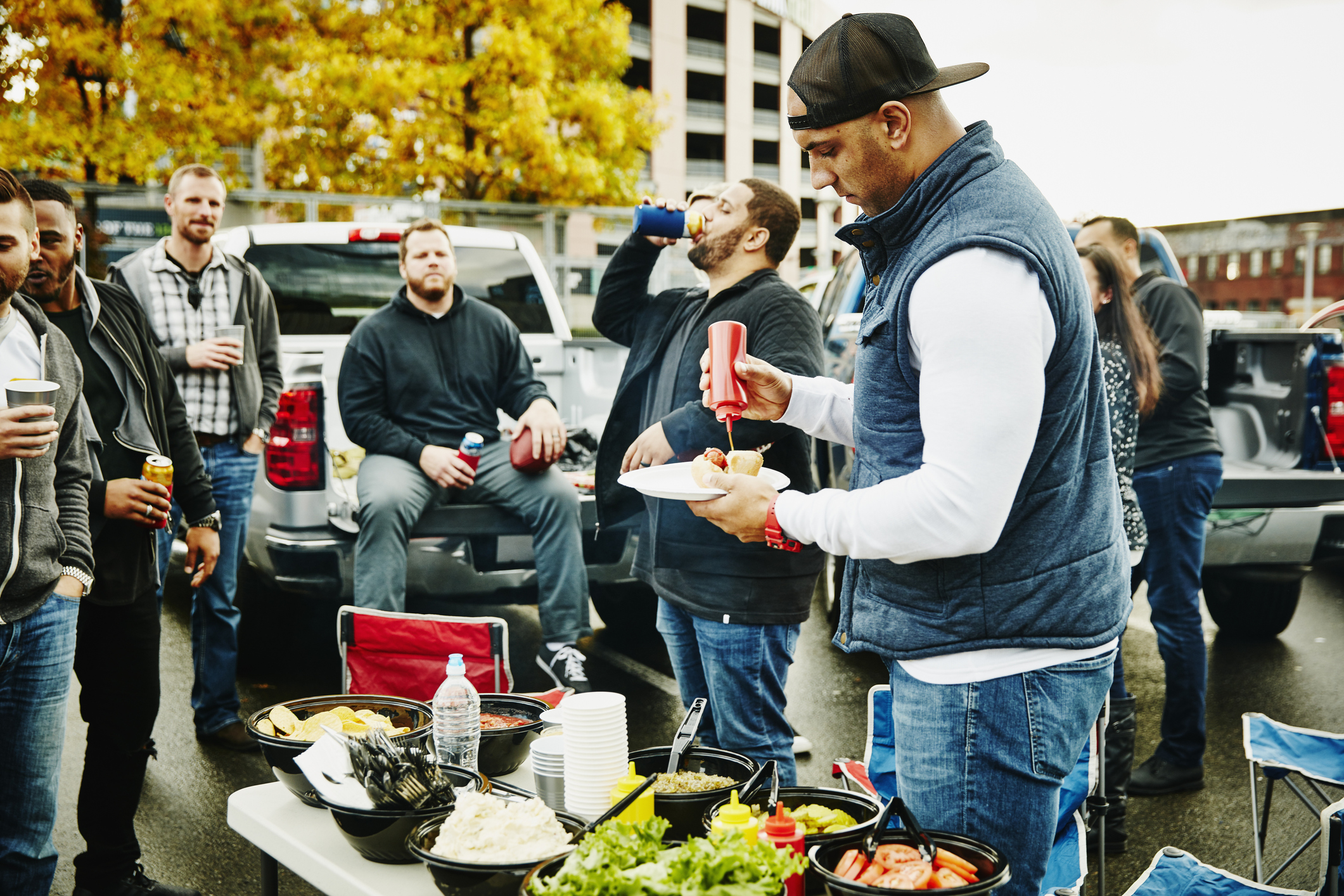 Man putting ketchup on hot dog during tailgating party in stadium parking lot before football game