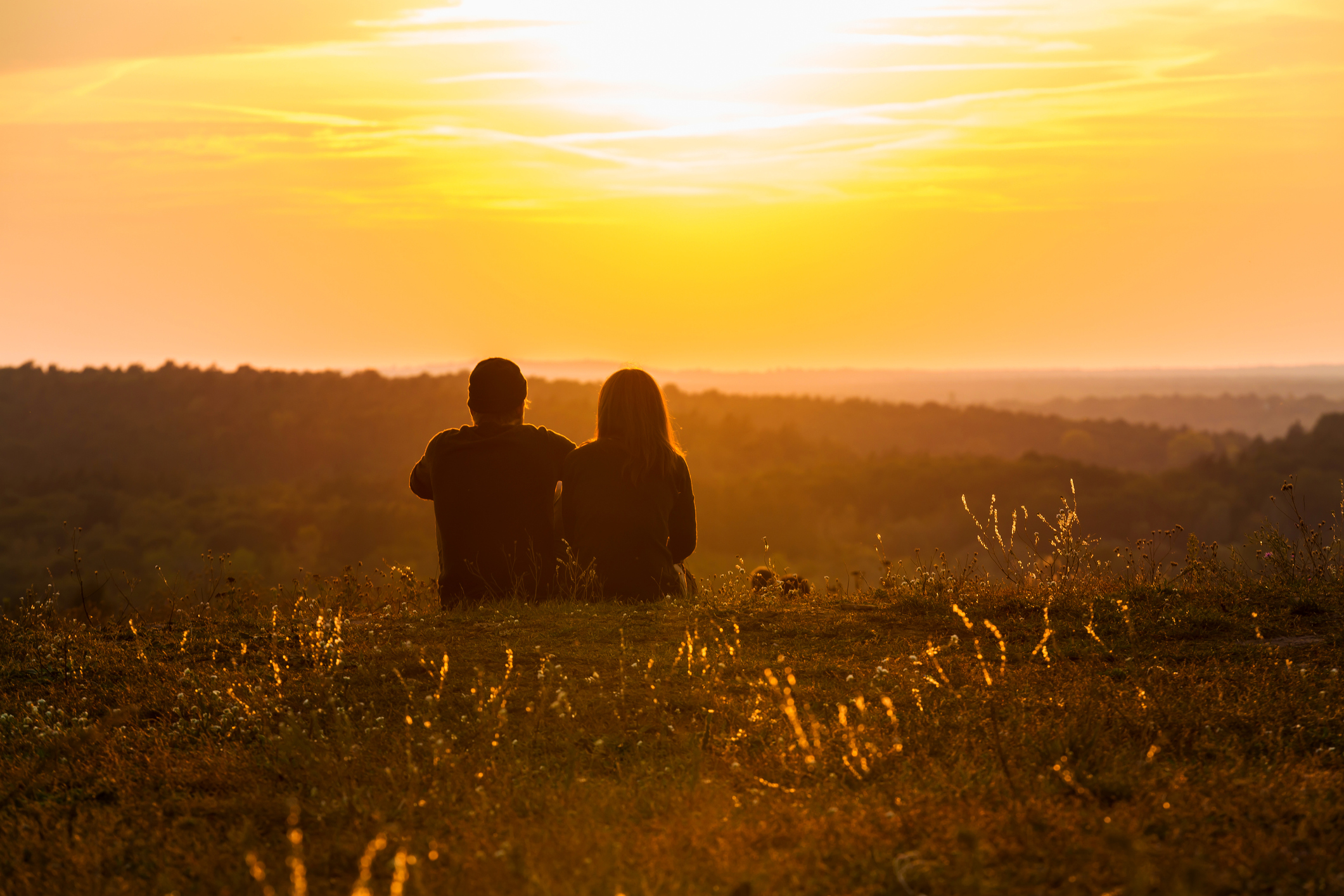 A couple sitting in the grass, enjoying the beautiful sunset.