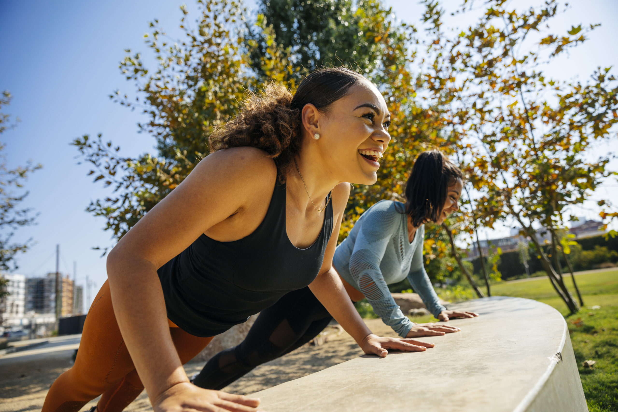 Cheerful women doing push-ups on retaining wall at park