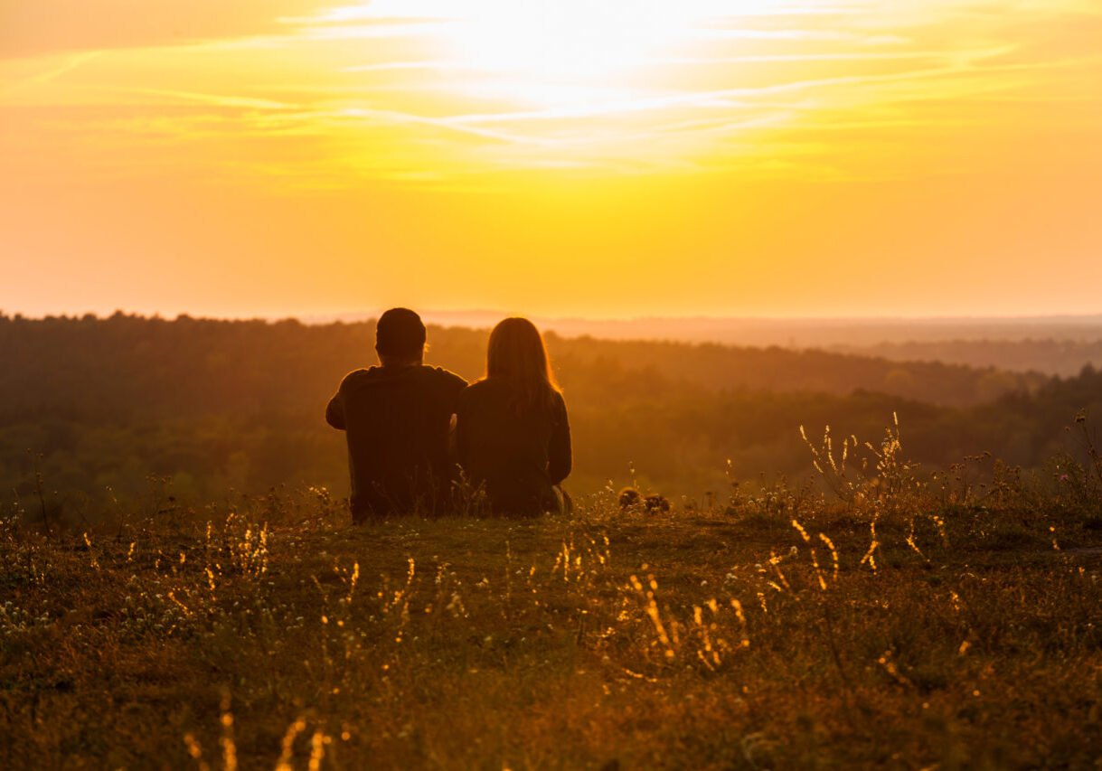 A couple sitting in the grass, enjoying the beautiful sunset.