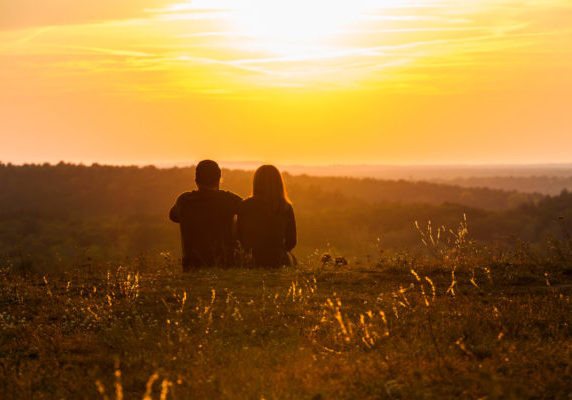 A couple sitting in the grass, enjoying the beautiful sunset.