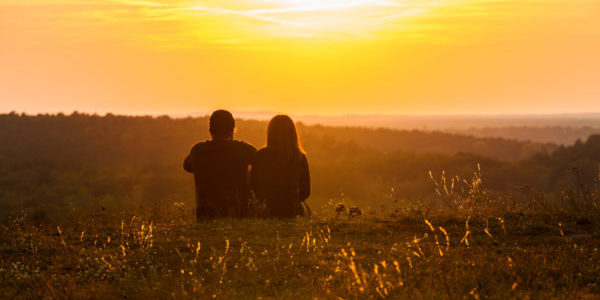 A couple sitting in the grass, enjoying the beautiful sunset.