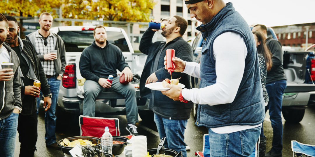 Man putting ketchup on hot dog during tailgating party in stadium parking lot before football game