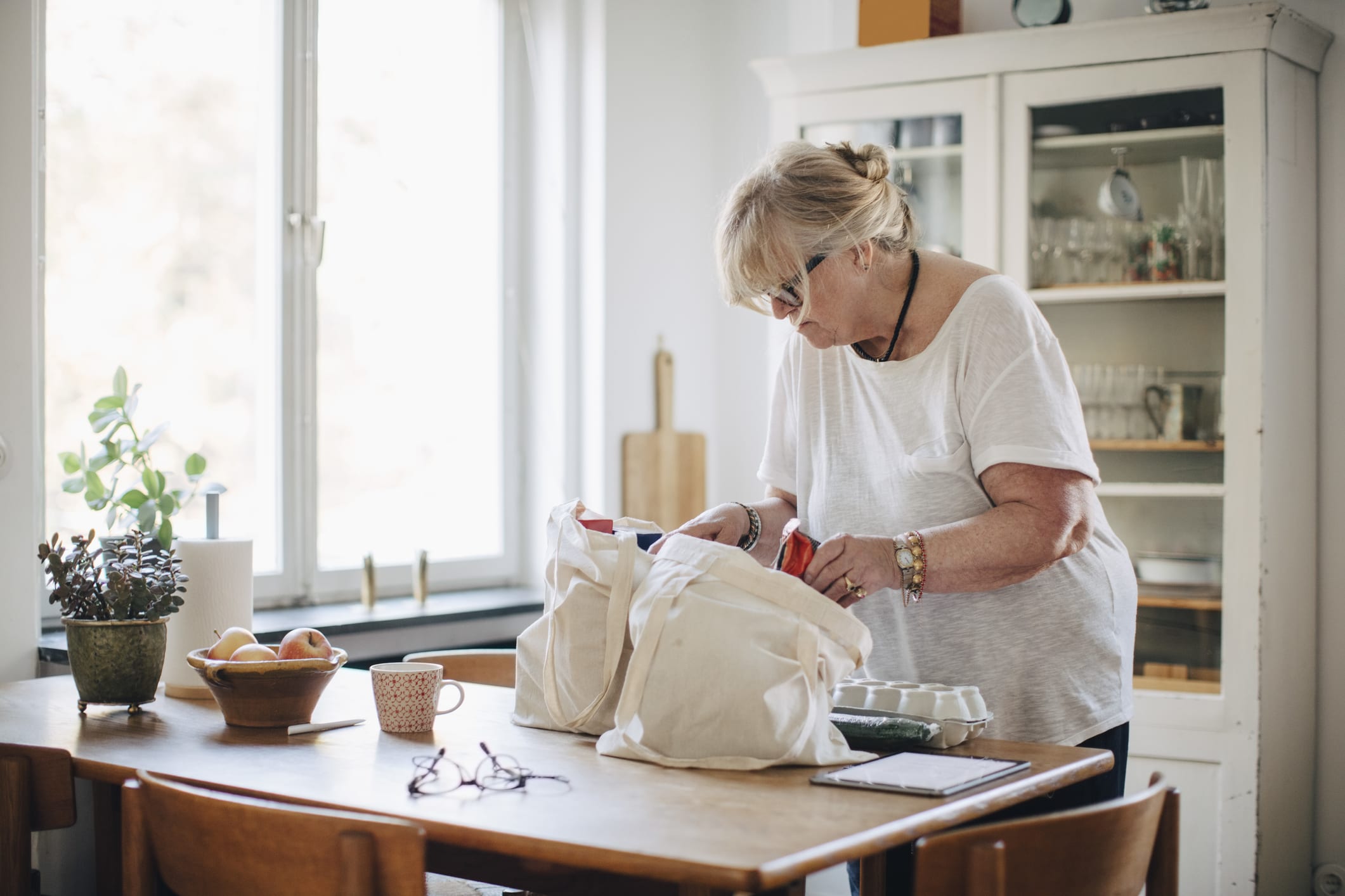 Senior woman removing groceries from shopping bag in kitchen at home