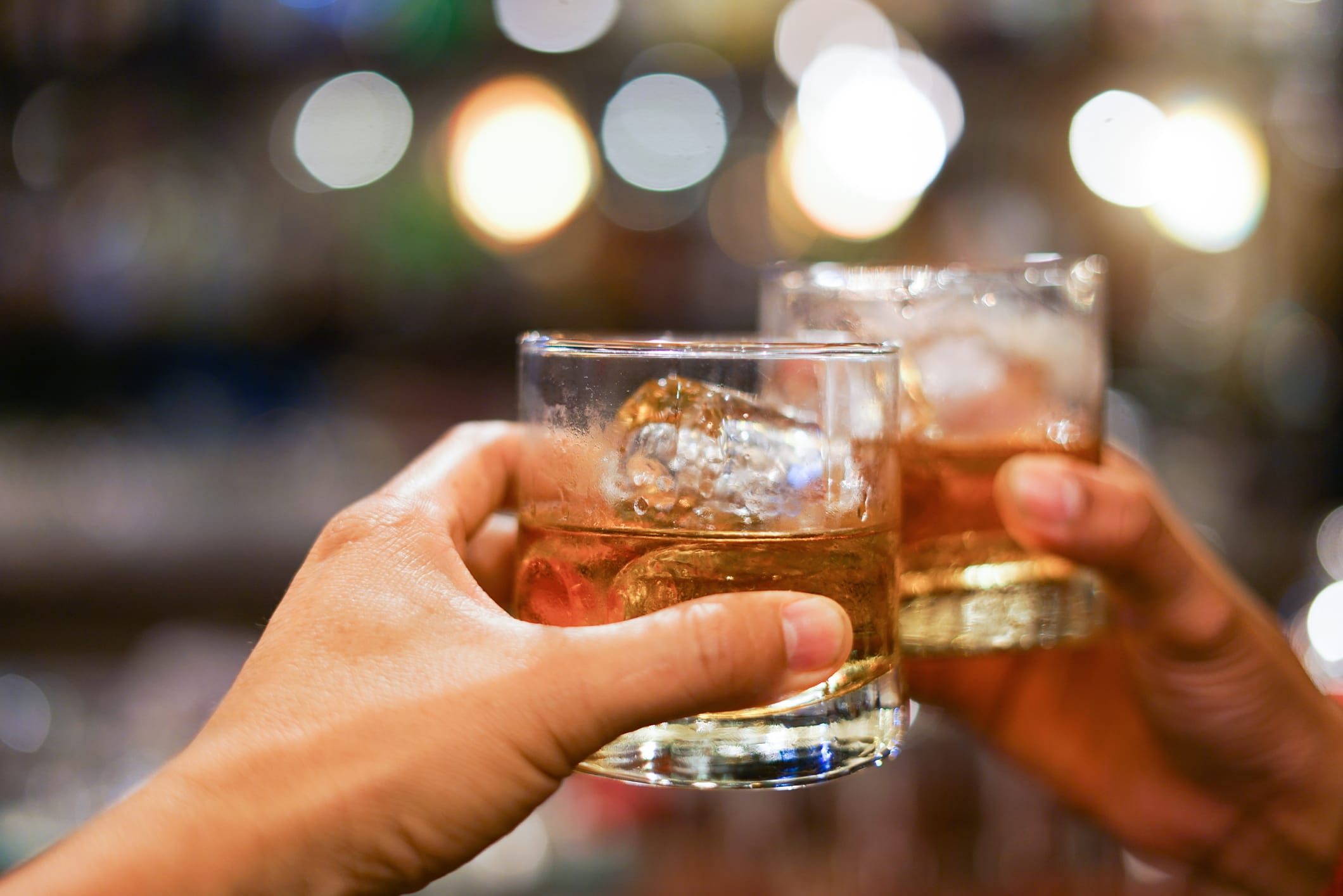 two men clinking glasses of whiskey drink alcohol beverage together at counter in the pub