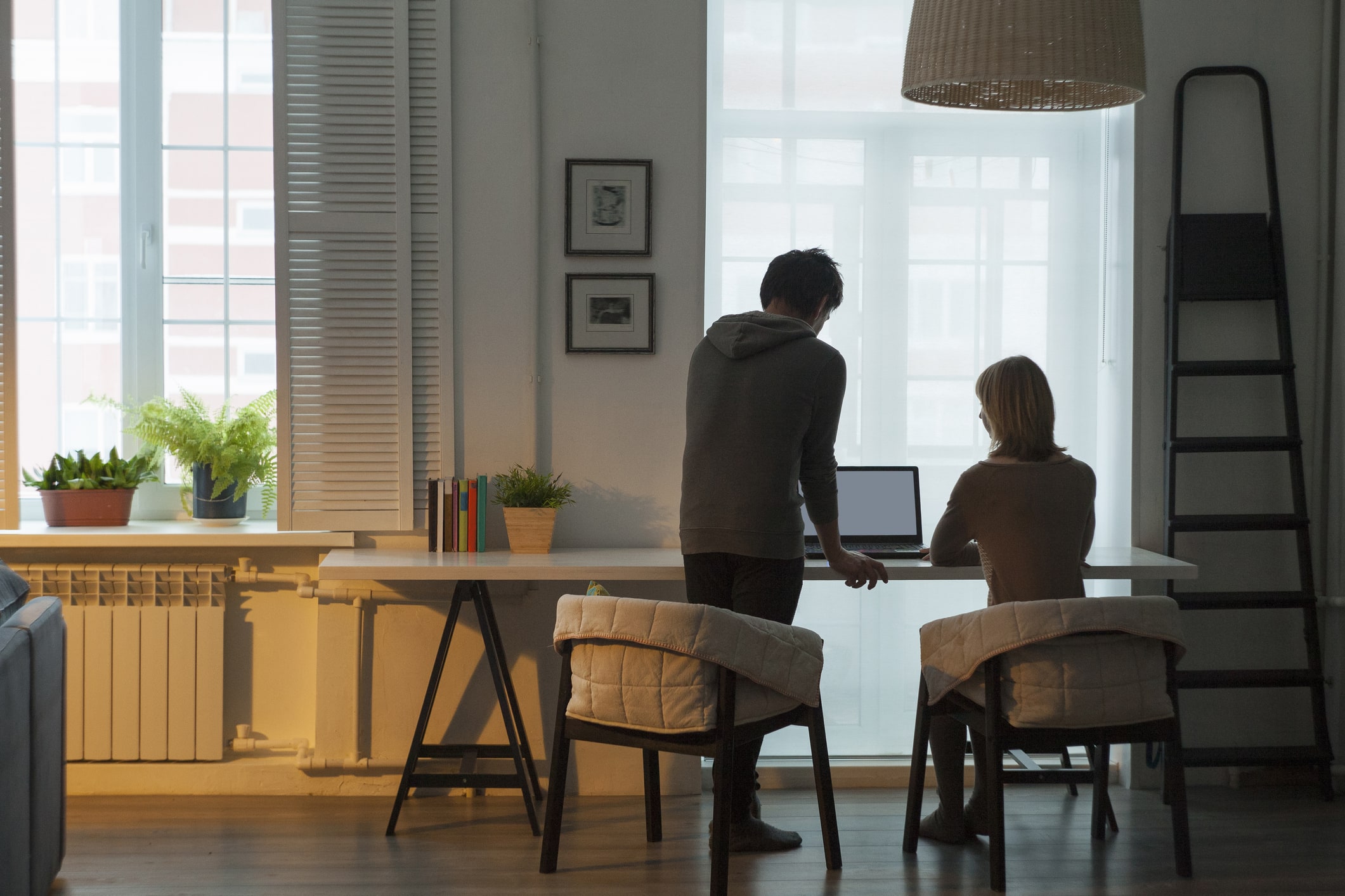 Rear view of mid adult couple using laptop at table in front of window