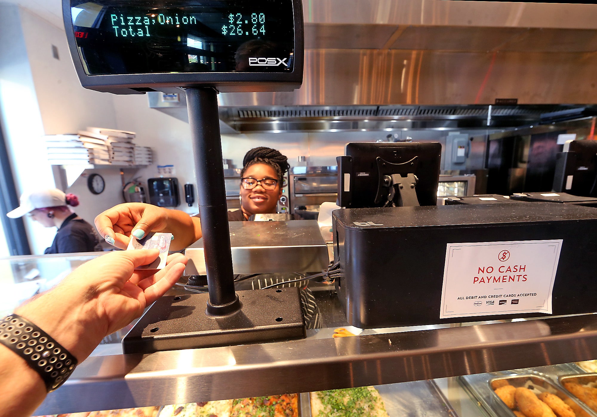 Semaj White takes a credit card at Bonci Pizza on Julia Street, one of several area businesses that do not accept cash.
(Photo by Michael DeMocker)