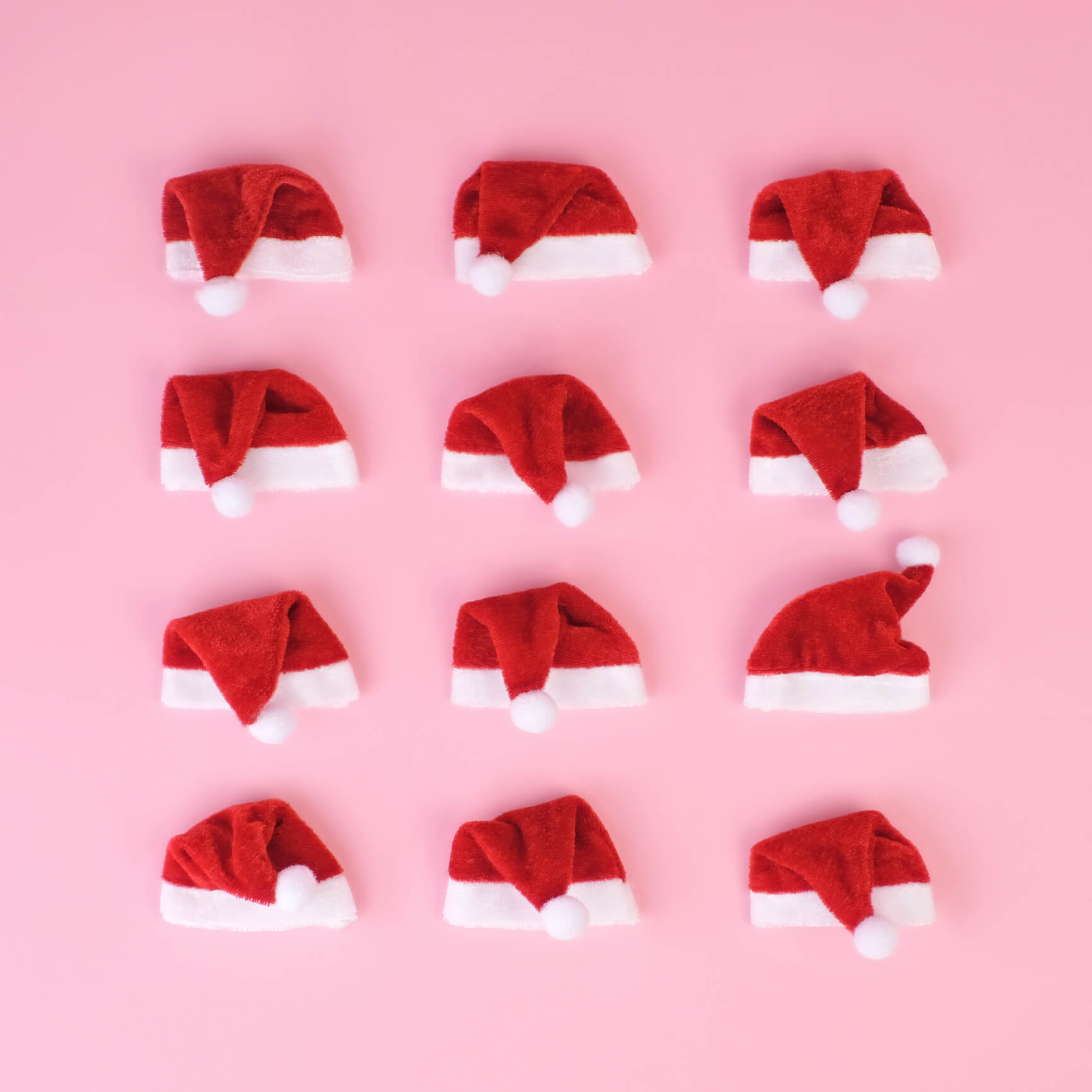 Miniature red Santa hats arranged in a grid on a pink background.