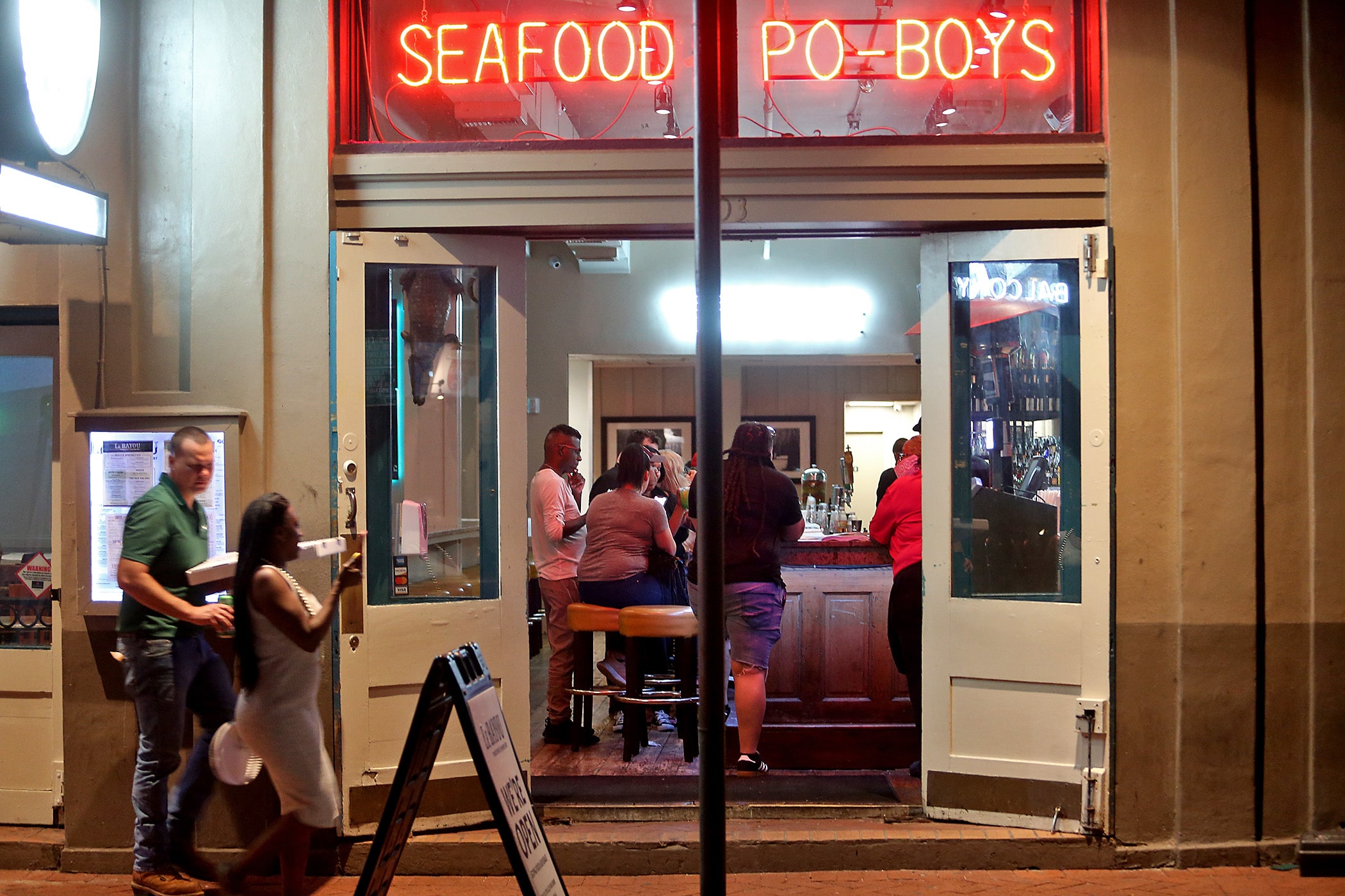 Customers walk down Bourbon Street in the French Quarter with take-out pizza, passing a restaurant with a crowded bar on the first evening of Phase One of the re-opening of New Orleans during the pandemic. Photographed on Saturday, May 16, 2020. (Photo by Michael DeMocker)