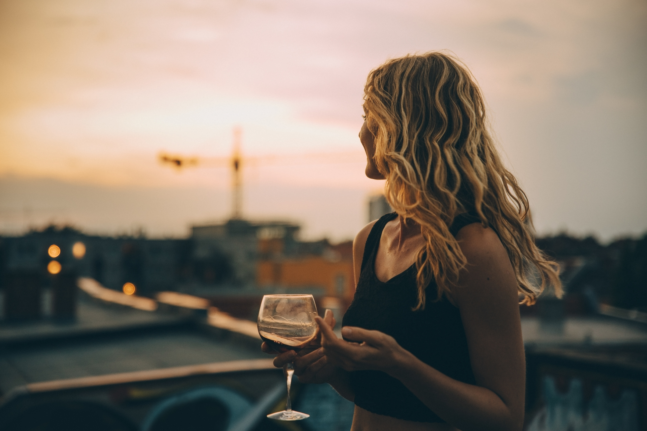 Thoughtful young woman having wine while looking away on terrace during rooftop party at sunset