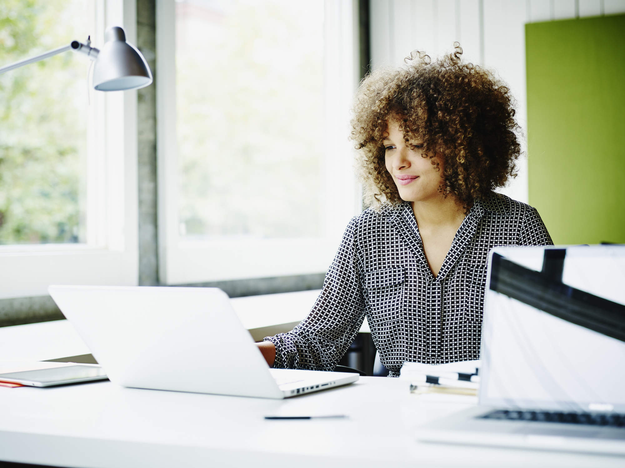 Smiling businesswoman sitting at workstation in office working on project on laptop