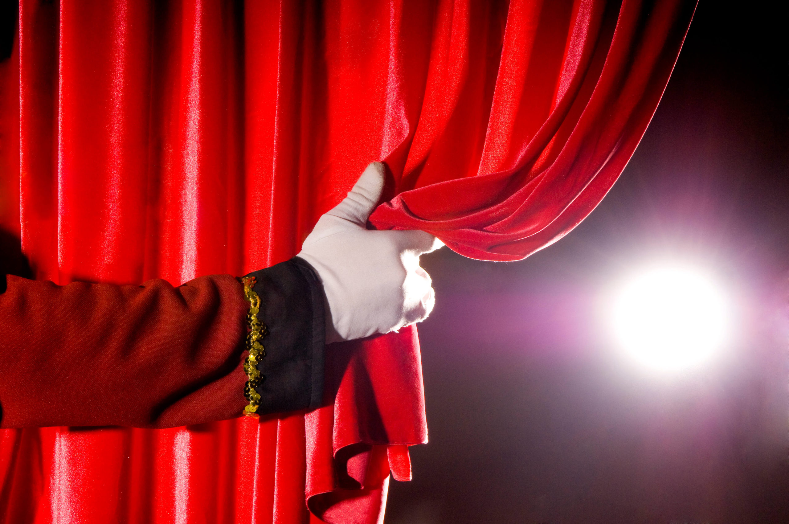 usher pulls open red curtain to reveal theater lighting...some noise visible.