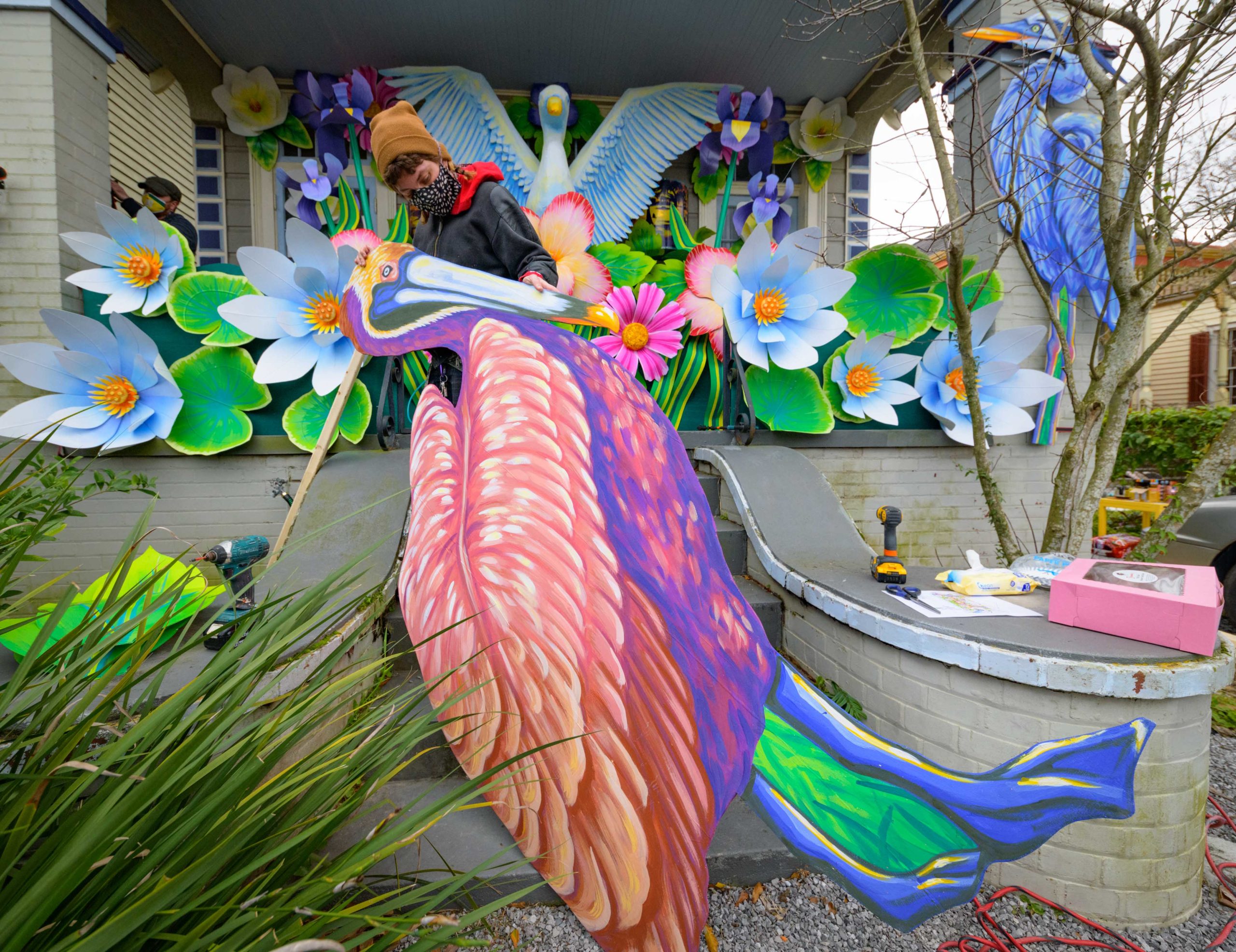 Mardi Gras float artists Chelsea Kamm, brown hat, Joey Mercer, yellow mask, and Travis Keene, purple hoodie, help construct a house float designed by Caroline Thomas, enjoying a piece of pink King Cake, for ÒHire a Mardi Gras ArtistÓ a project of the Krewe of Red Beans. Residents who live in Orleans Parish and donate to the project are entered into the raffle to get one of the house floats and this float went to a raffle winner in the Fairgrounds neighborhood of New Orleans. The grassroots effort hopes to build 40 house floats for every $15,000 donated. The donations go towards supplies and hiring float artists, many who are out-of-work because of the cancellation of Mardi Gras and Carnival parades due to the COVID-19 pandemic. In addition to the three artists putting the float together many other artists helped sculpt and construct the birds and flowers for the float. This float celebrates local wildlife and is called ÒThe Birds of Bulbancha.Ó Bulbancha is Choctaw word meaning Òplace of many tongues,Ó and was the name the indigenous people called the trading port in what is now New Orleans before the arrival of European colonists. The birds include a Great Egret, the centerpiece sculpture, and panels of a Great Blue Heron, Brown Pelican, Whooping Crane, and Roseate Spoonbill. Photos by @MattHintonPhoto for @VeryLocalNOLA
#HireAMardiGrasArtist @Redbeansparade #KreweofRedBeans @c_to_the_line #NewOrleans #Louisiana #Carnival #neworleanslouisiana #nolalife #herenowlouisiana #gonola #onetimeinnola #itsyournola #showmeyournola #nola #followyournola #exploreneworleans #ilovenola #VLNOLAÊ#VLNOLAMardigrasÊ#kreweofhousefloatsÊ#mardigras2021 @kreweofhousefloats