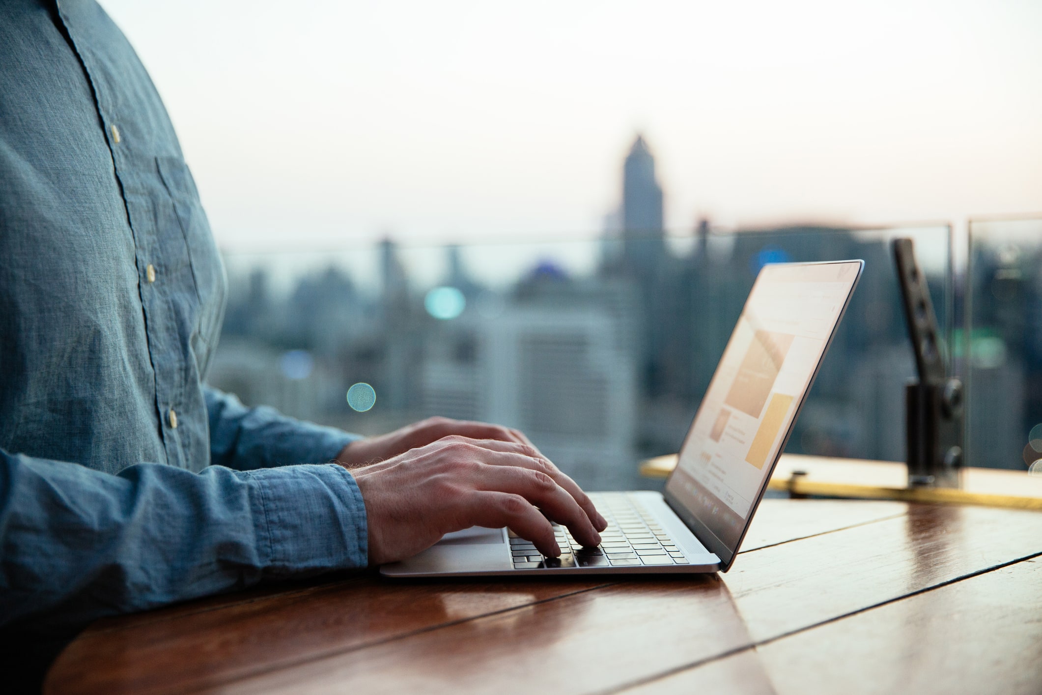 Man typing on laptop keyboard with city background