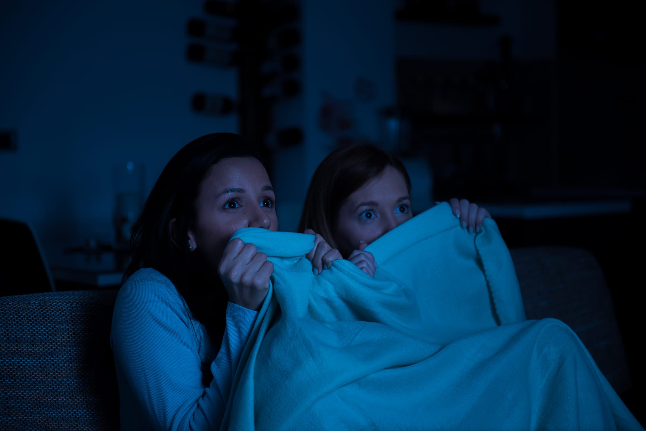 Two women watching horror movie on a tv together, sitting on a sofa with blanket, scared, lesbian couple, girlfriends, homosexual couple, friends