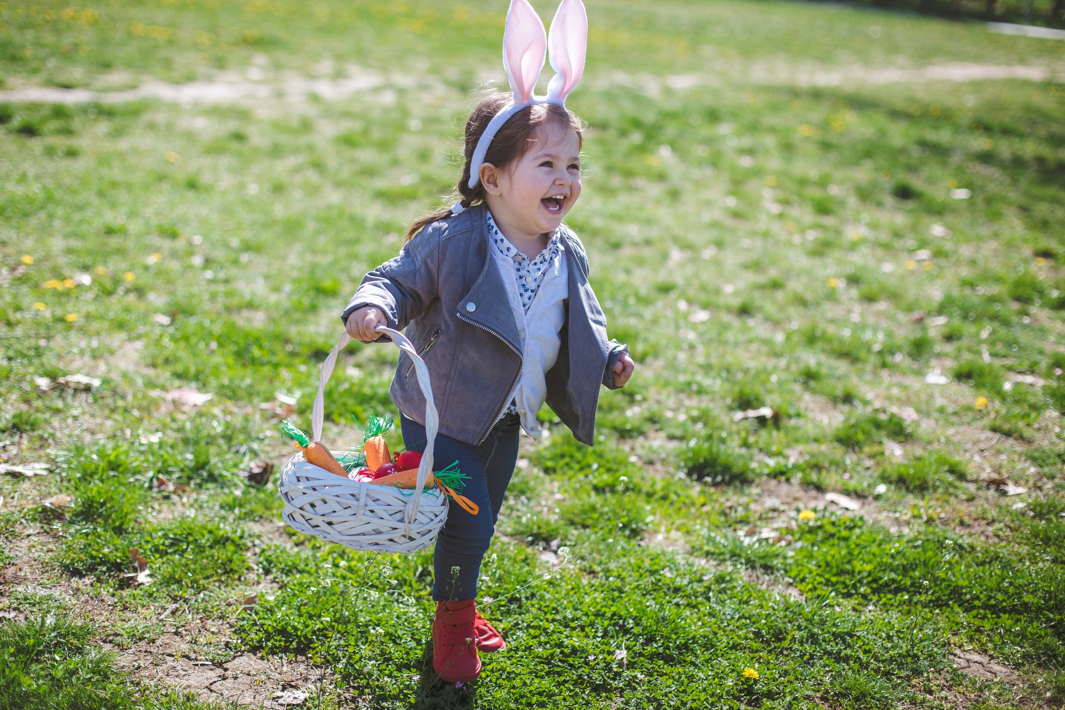 Cute toddler girl wearing a bunny ears at the park during Easter celebration, and hunting for Easter eggs.