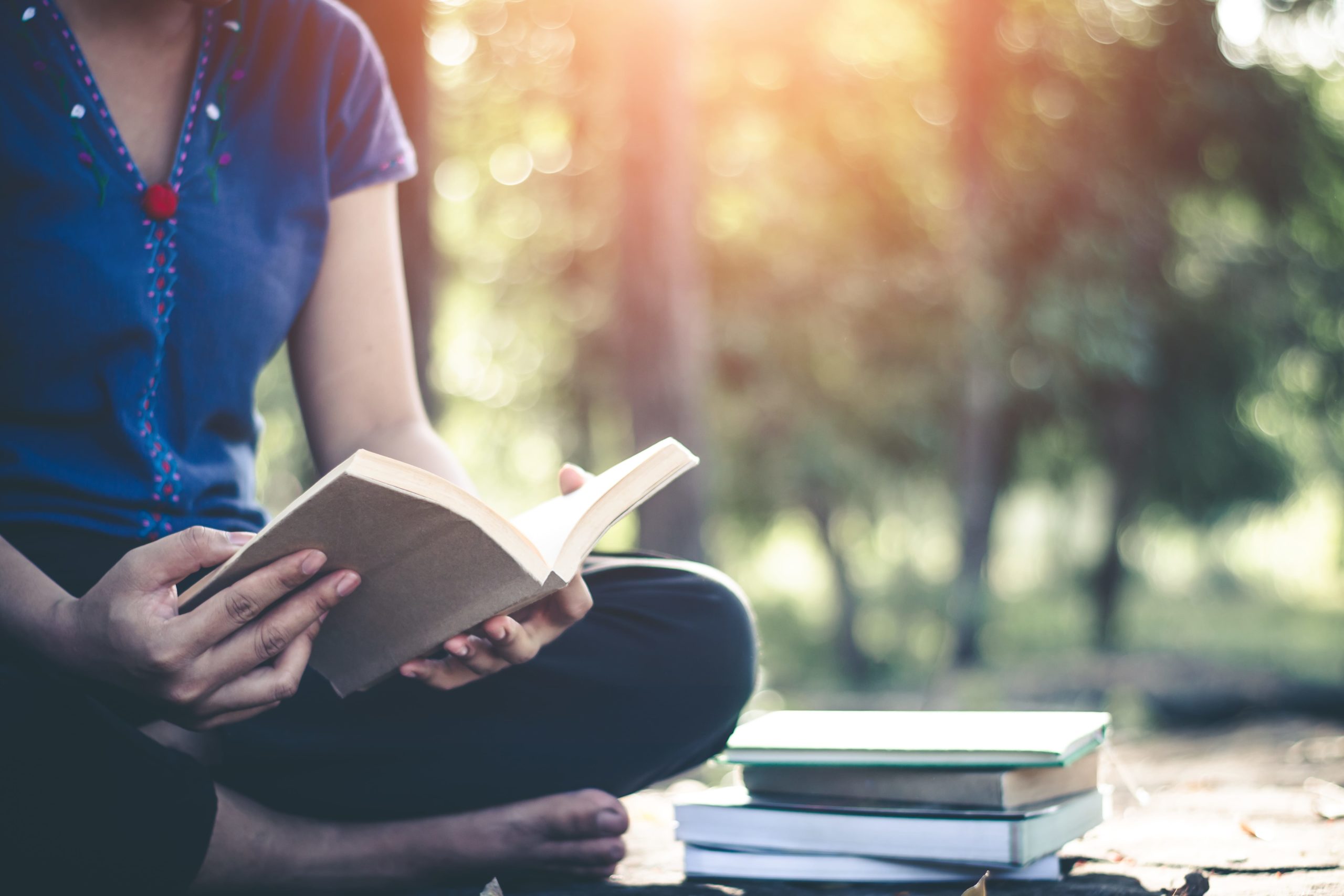 Low Section Of Woman Turning Book Pages While Sitting On Field