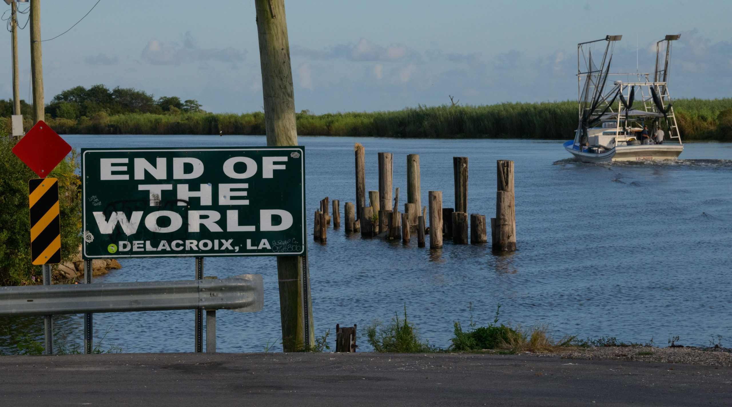 A sign for the End of the World Marina, that was destroyed by Hurricane Katrina, is seen in Delacroix, La. Tuesday, Oct. 15, 2019 as shrimp boat passes. Delacroix was settled by Islenos from the Canary Islands who spoke Spanish and near and interacted with Filipino settlers at the nearby St. Malo platform on Lake Borgne in 1800s. Photo by Matthew Hinton