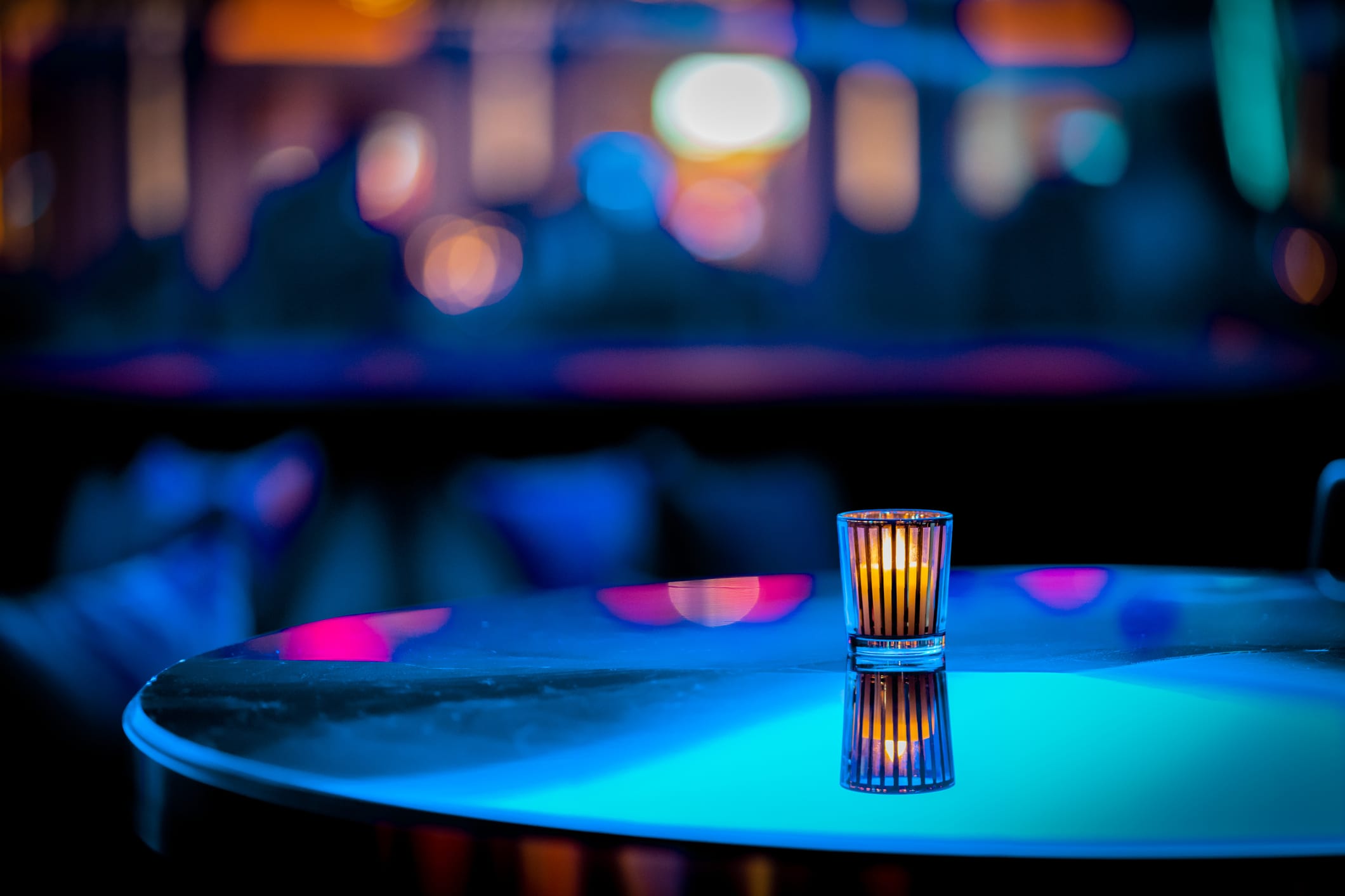 Minimalistic or abstract candle on table at a nightclub with out of focus background -- teal, blue and pink bokeh